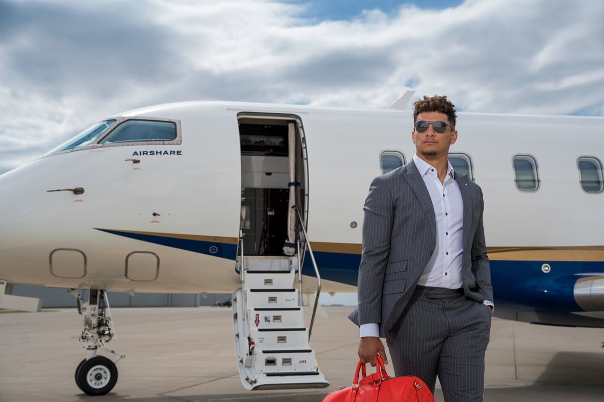 Two-time NFL MVP, Patrick Mahomes standing in a gray pinstriped suit, holding his travel bag in-front of an Airshare Challenger 3500